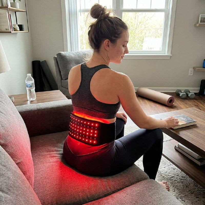 Woman relaxing on couch wearing Lumovex red light therapy belt