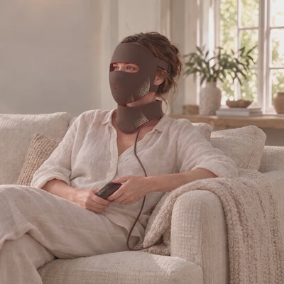Woman relaxing on a sofa wearing the Lumovex Spectrum Pro mask and neck red light therapy device